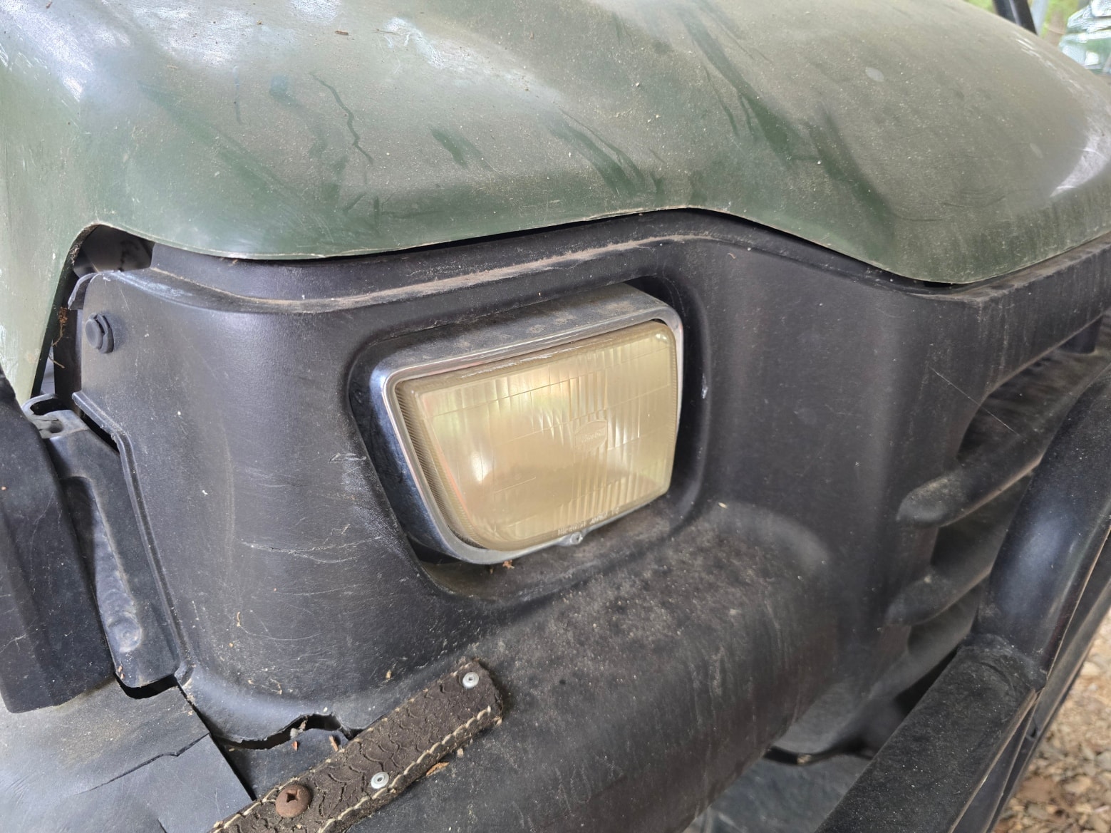 Yellowed, hazy rectangular headlight on green John Deere utility vehicle before restoration